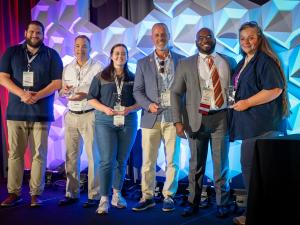 Six Richard Lichtenfelt Award winners stand in a row, smiling with their awards