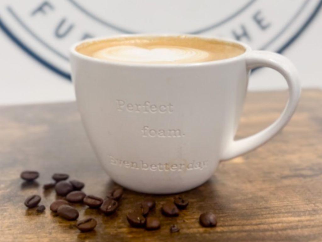 Latte in a mug from The Bistro with coffee beans scattered beside it